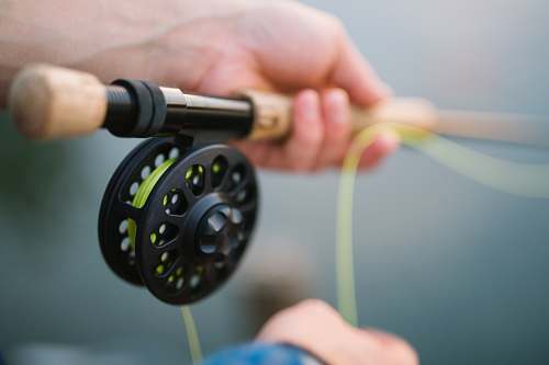 fly fishing person holding black and brown fishing rod reel
